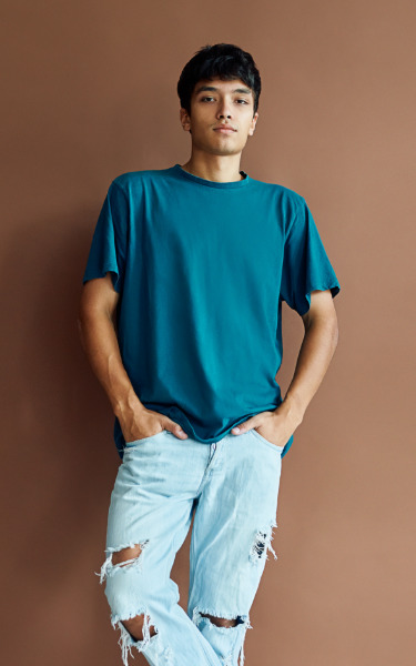 A young man leaning against a brown wall next to a list of key concerns among people with hemophilia