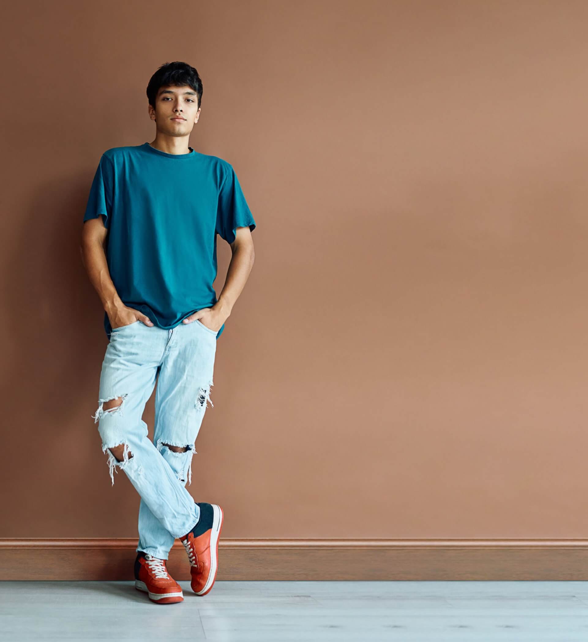 A young man leaning against a brown wall next to a list of key concerns among people with hemophilia